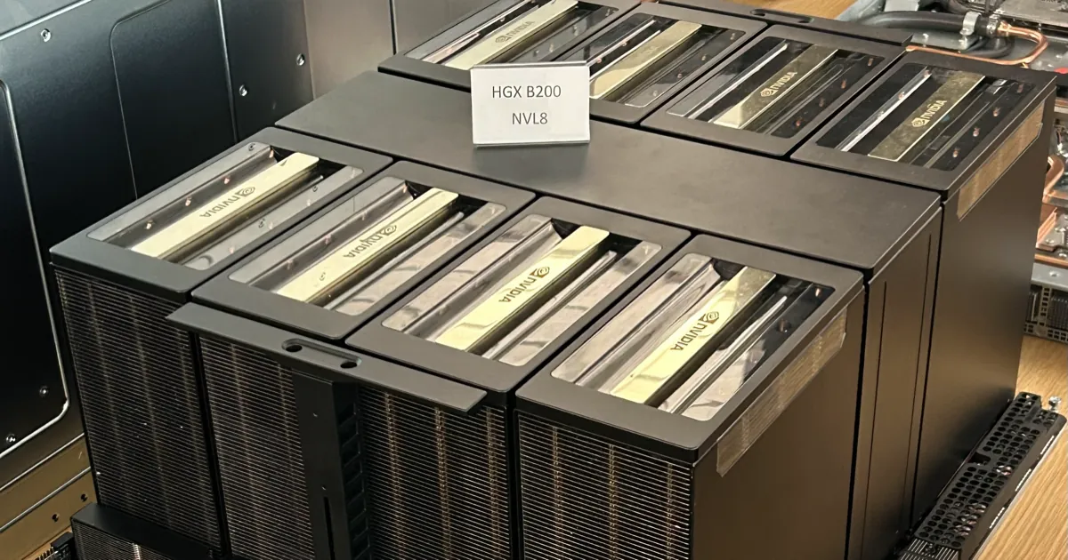 An Nvidia HGX B200 board with eight large GPU heatsinks and a printed label, on a display table