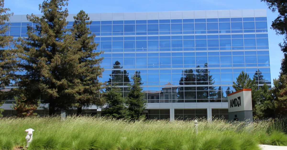 AMD's glass office building at 2485 Augustine Drive in Santa Clara, behind tall grass and redwoods, with an AMD sign on the right