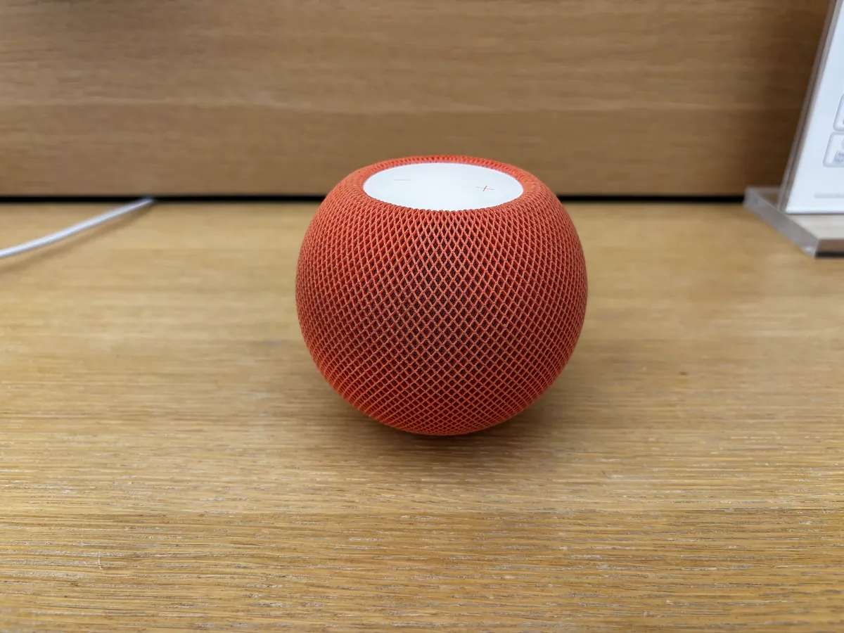An orange HomePod mini, the current model, on a wooden shelf in a store