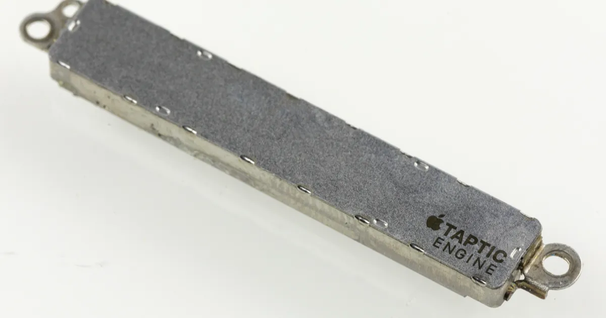 An Apple Taptic Engine vibration module from an iPhone 6s, a thin metal bar with mounting tabs at each end