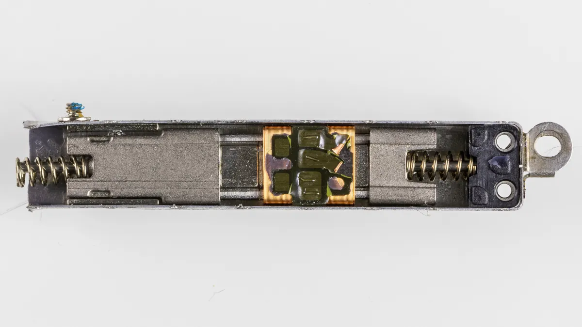 An opened iPhone 6s Taptic Engine showing a sliding metal mass between two coil springs, with a copper coil in the middle