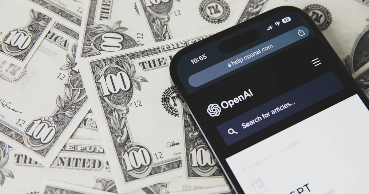 A phone showing OpenAI's help center lying on a spread of prop US$100 bills