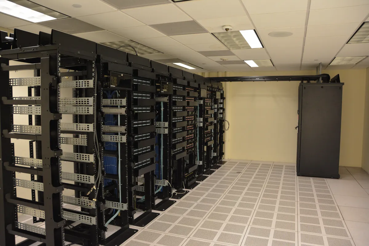Rows of black server racks with blue network cabling in a data center with a raised tile floor