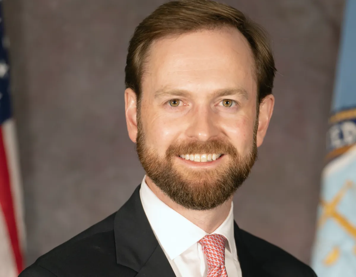 Official portrait of Andrew Ferguson, now FTC chairman, smiling in a dark suit and pink tie in front of the US flag