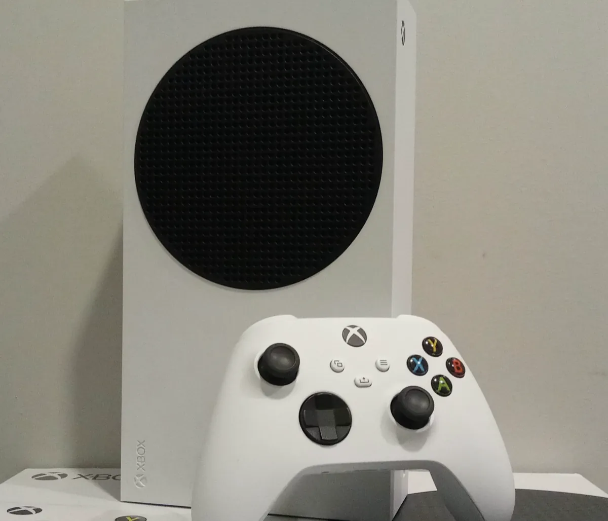 A white Xbox Series S console standing upright behind a white Xbox Wireless Controller