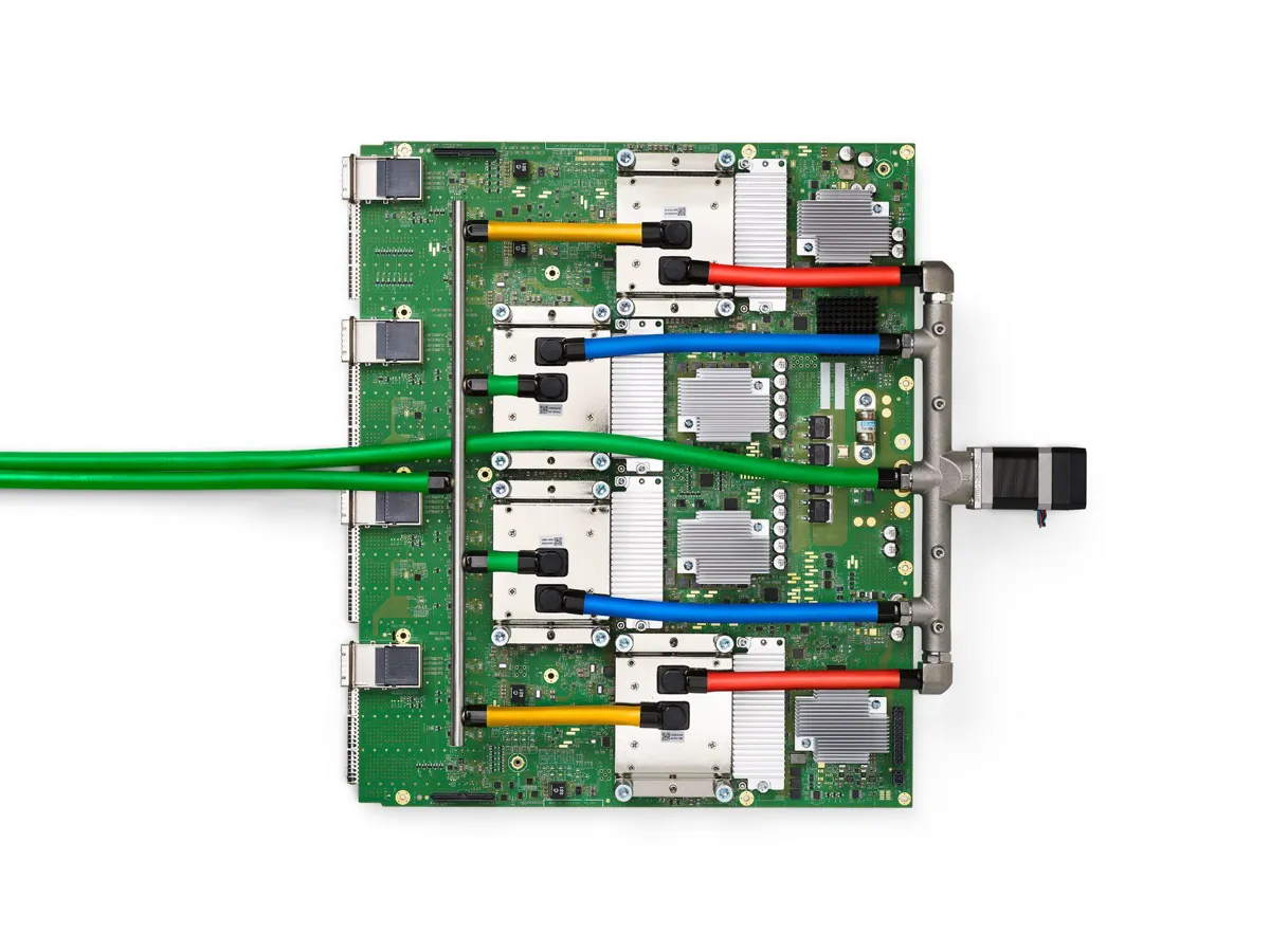 A Google TPU v4 circuit board with four chip packages linked by red, blue, yellow and green liquid-cooling hoses