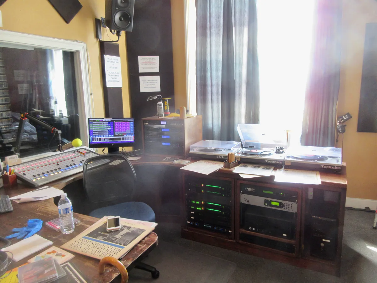 A radio station's on-air studio with a mixing desk, a microphone on a boom arm, a computer screen and three turntables