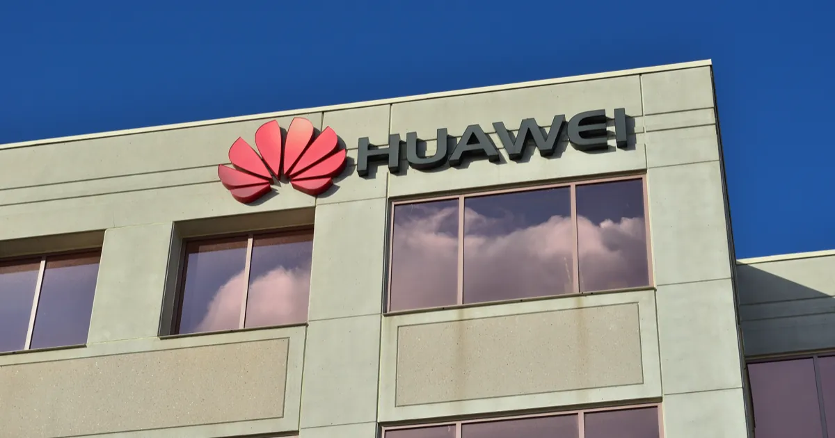 The red Huawei logo and name on the facade of a Huawei office building under a deep blue sky