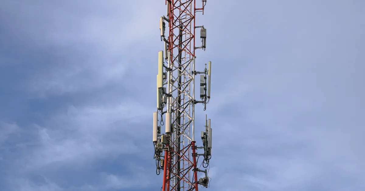 A red and white cellular tower with panel antennas against a cloudy sky in Ciudad del Carmen, Campeche, Mexico