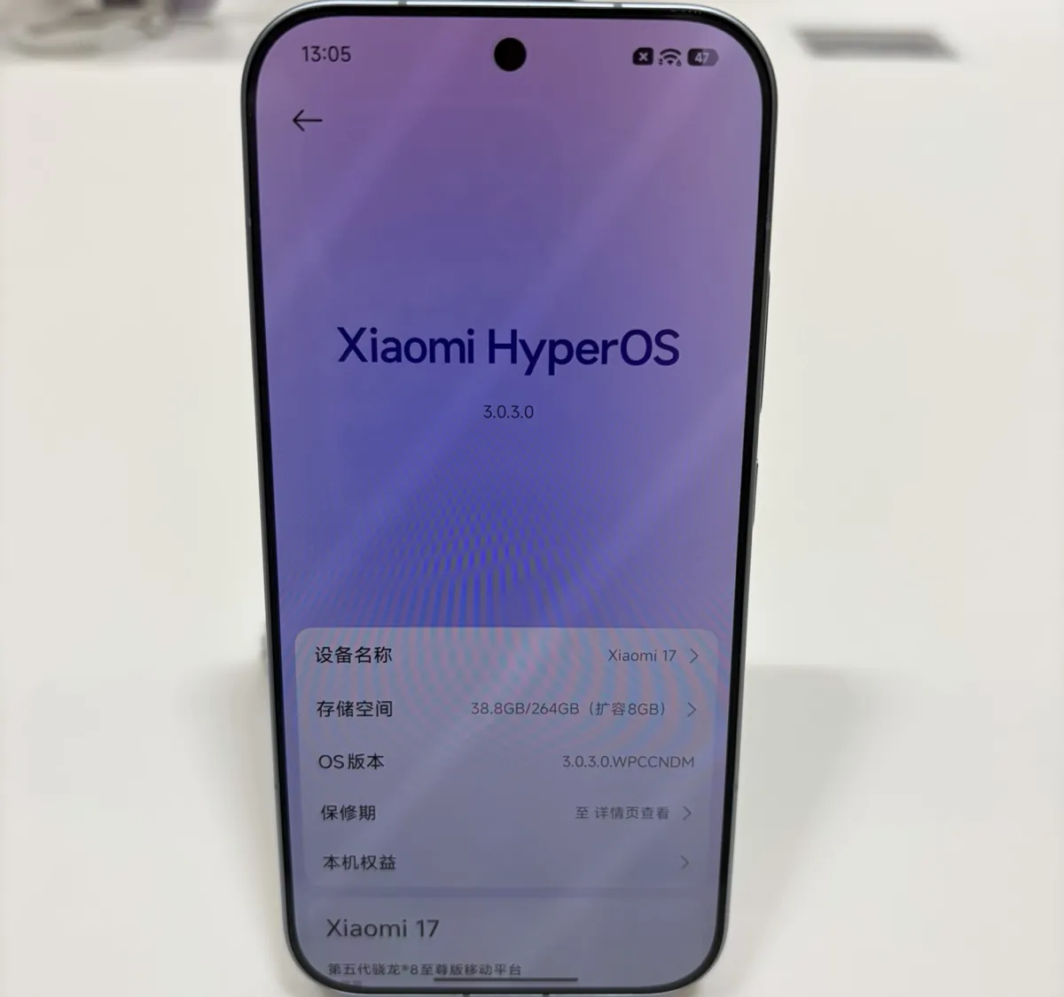 A Xiaomi 17 on a store display stand showing its About phone screen in Chinese, with Xiaomi HyperOS 3.0.3.0