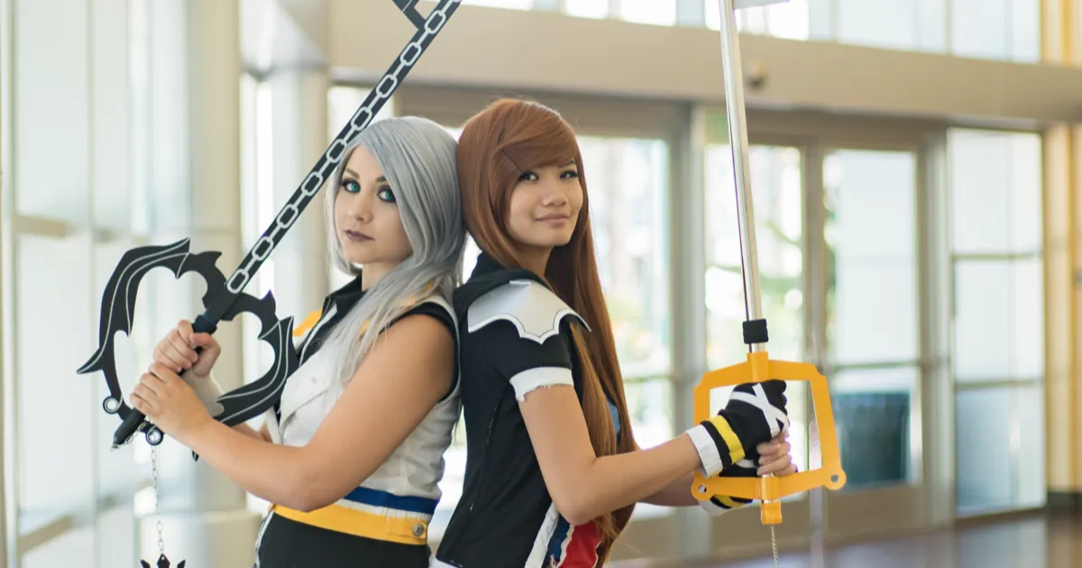 Two cosplayers dressed as Riku and Sora from Kingdom Hearts stand back to back holding their Keyblades