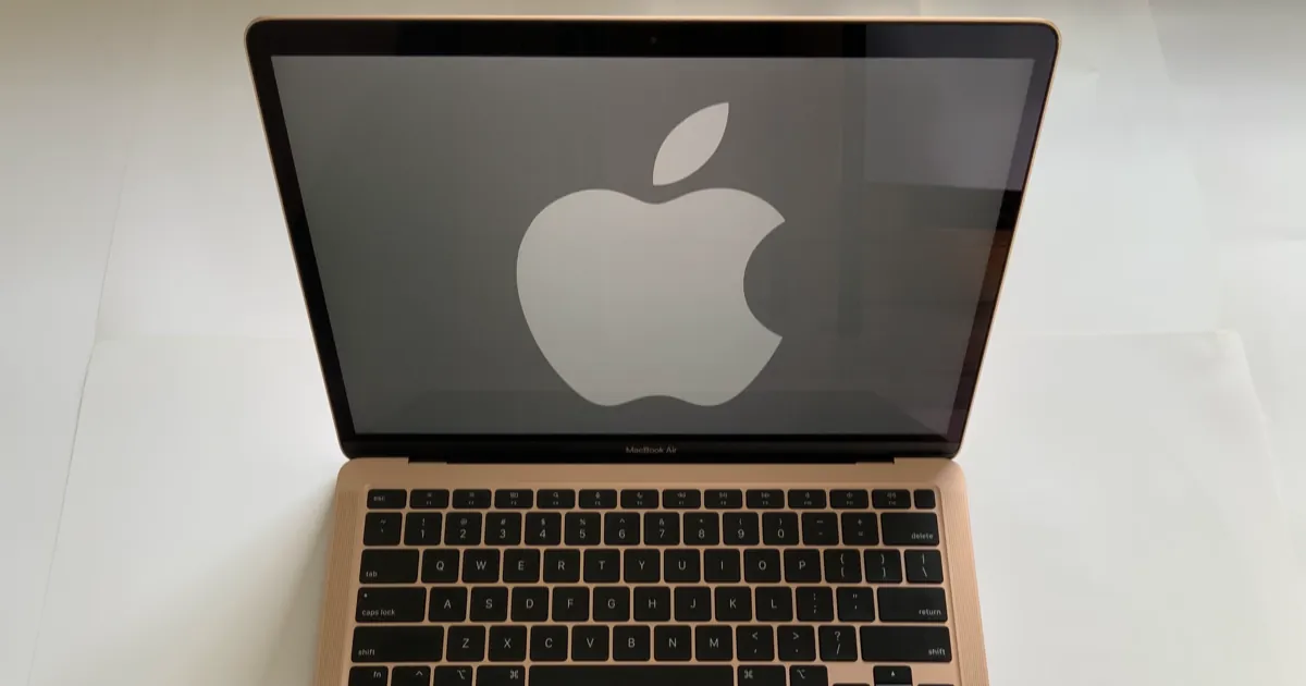 A gold MacBook Air open on a white table, its screen showing a large Apple logo above the keyboard