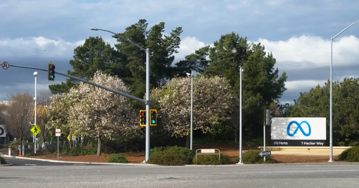 Meta's 1 Hacker Way sign with its blue infinity logo beside a road at the company's Menlo Park headquarters