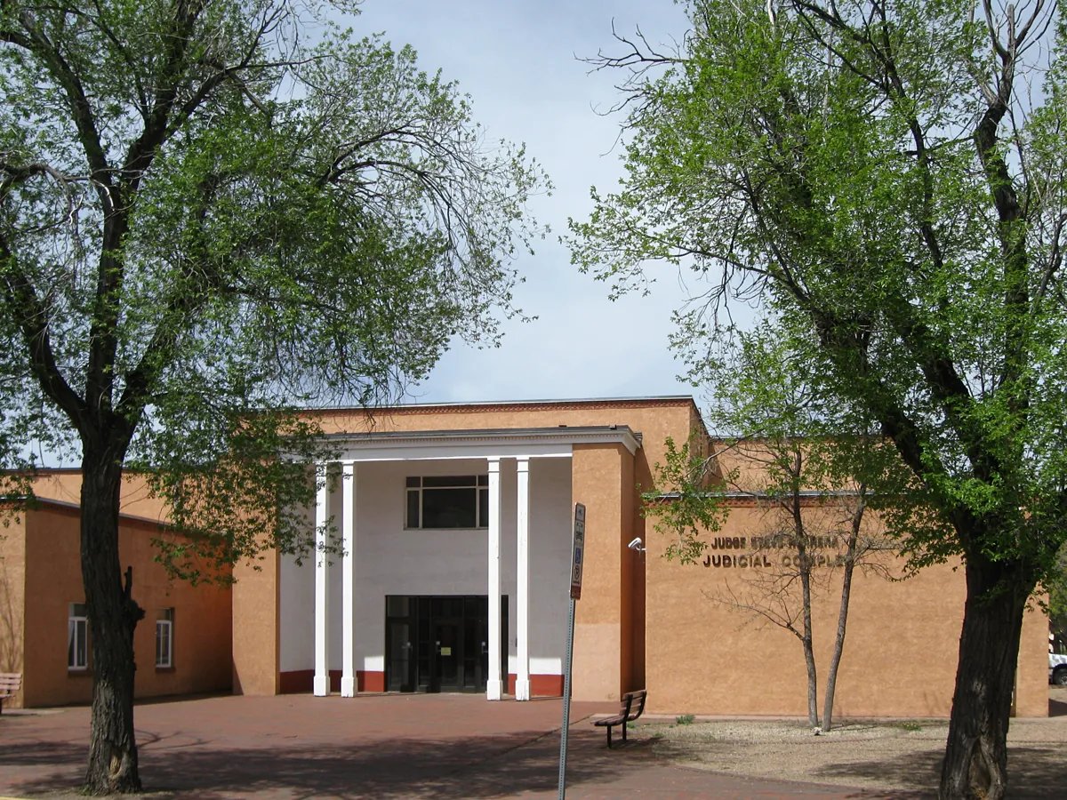 Tan stucco front of the Judge Steve Herrera Judicial Complex in Santa Fe, with white columns framed by two large trees