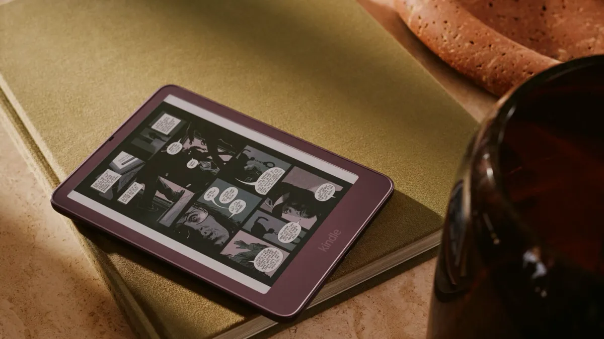 A Kindle Colorsoft in Fig showing a comic page in color, resting on a green book