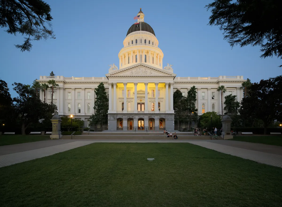 The California State Capitol in Sacramento at dusk, its dome lit from inside above a wide lawn