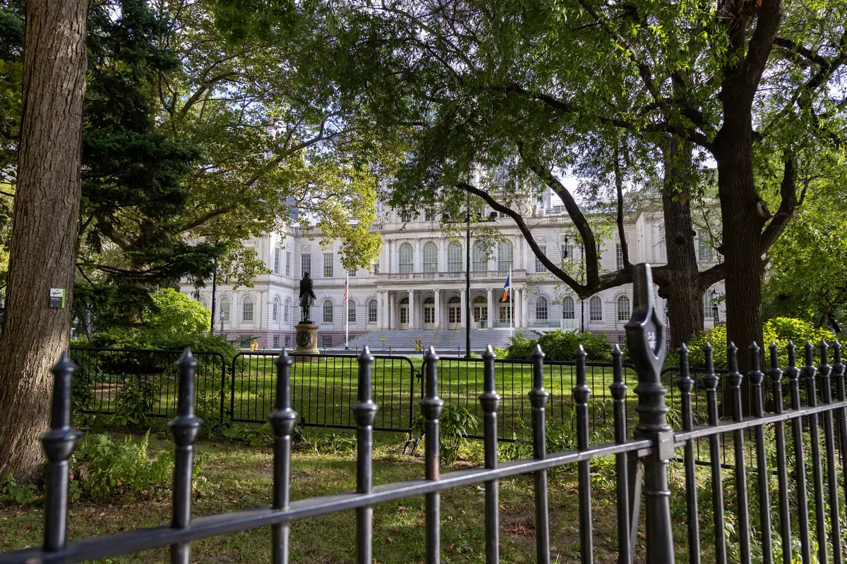 New York City Hall seen through the trees and iron fence of City Hall Park on a sunny day