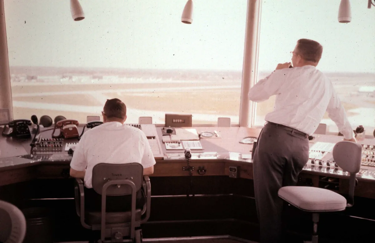 Two civilian air traffic controllers at the consoles of an airport control tower in Memphis, Tennessee, looking out over the airfield