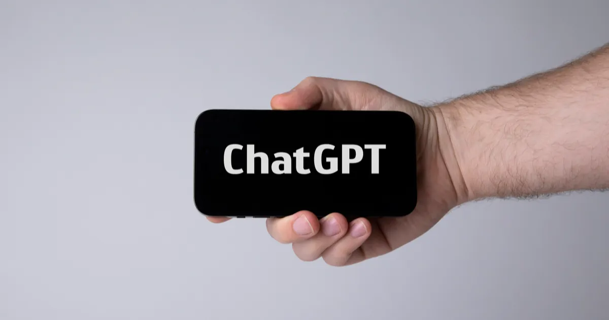 A hand holding a smartphone sideways with the word ChatGPT in white on a black screen