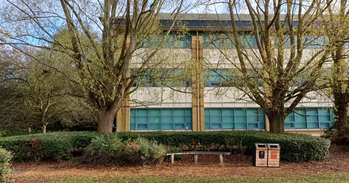 Jagex headquarters at 220 Cambridge Science Park in Cambridge, England, seen behind willow trees and a hedge