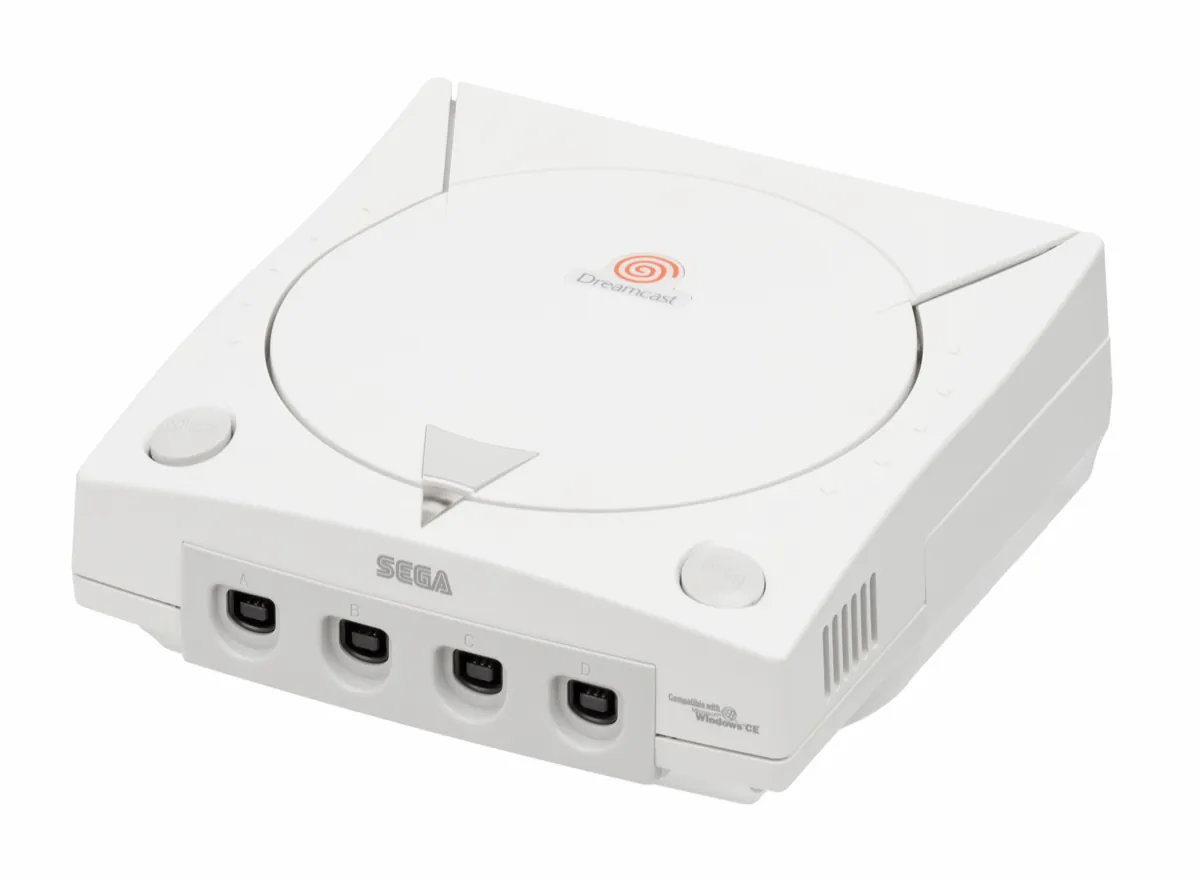 A white Sega Dreamcast console seen from the front, with four controller ports and the orange swirl logo on its lid