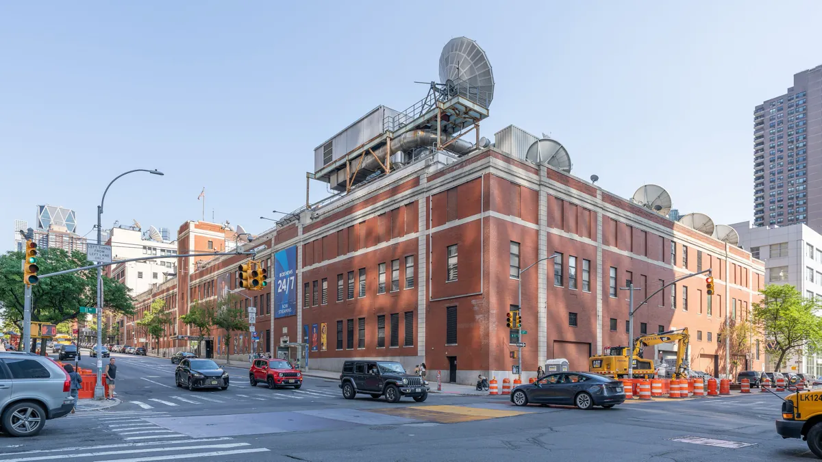 The red brick CBS Broadcast Center in New York, with satellite dishes on the roof and a CBS News 24/7 streaming banner on the wall