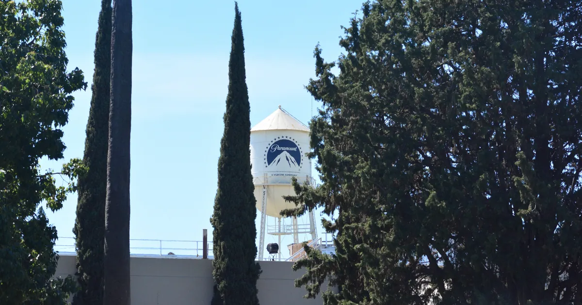 The Paramount water tower with its blue mountain logo rising behind tall cypress trees on the studio lot in Hollywood