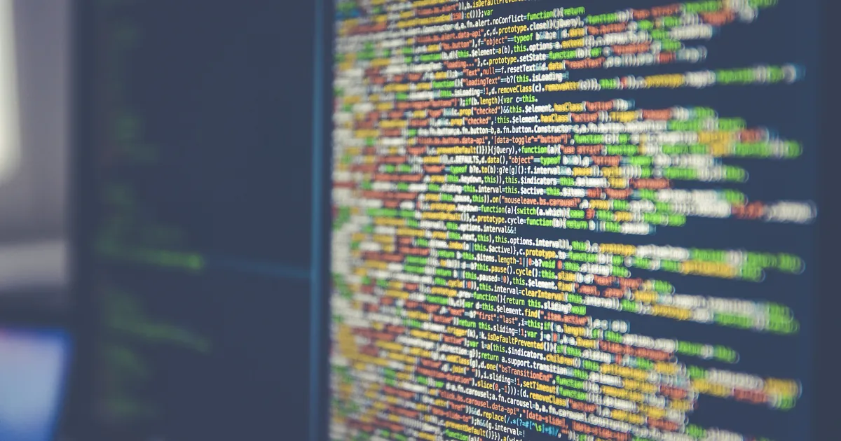 Close-up of a monitor full of colorful JavaScript source code, slightly out of focus at the edges