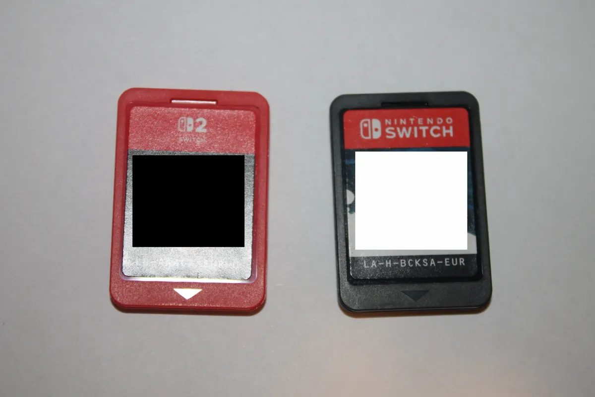 A red Nintendo Switch 2 game card next to a black original Nintendo Switch game card on a white surface, with their labels covered