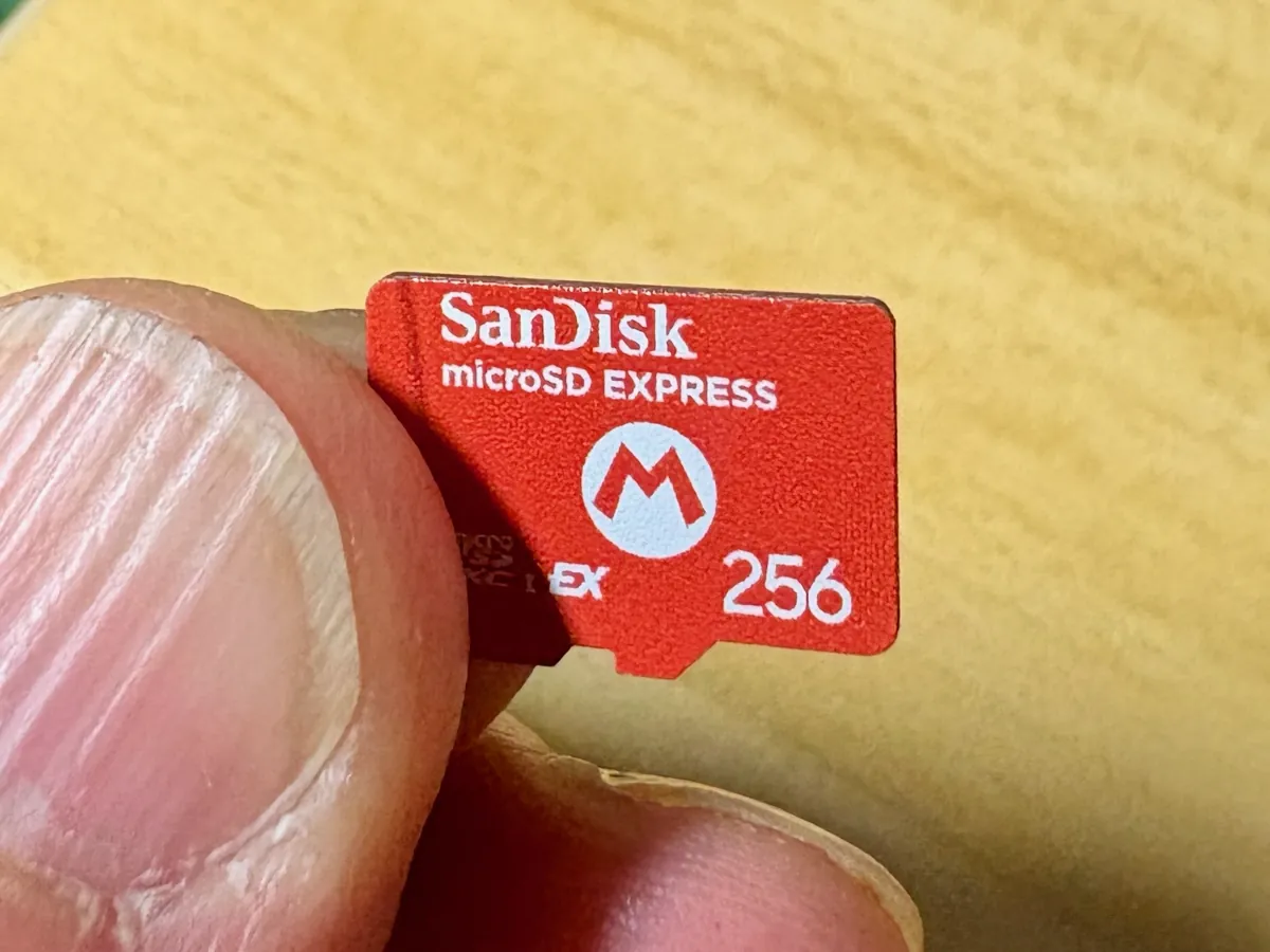 A red 256 GB microSD Express card held between two fingers, with microSD EXPRESS and an EX mark printed on the front