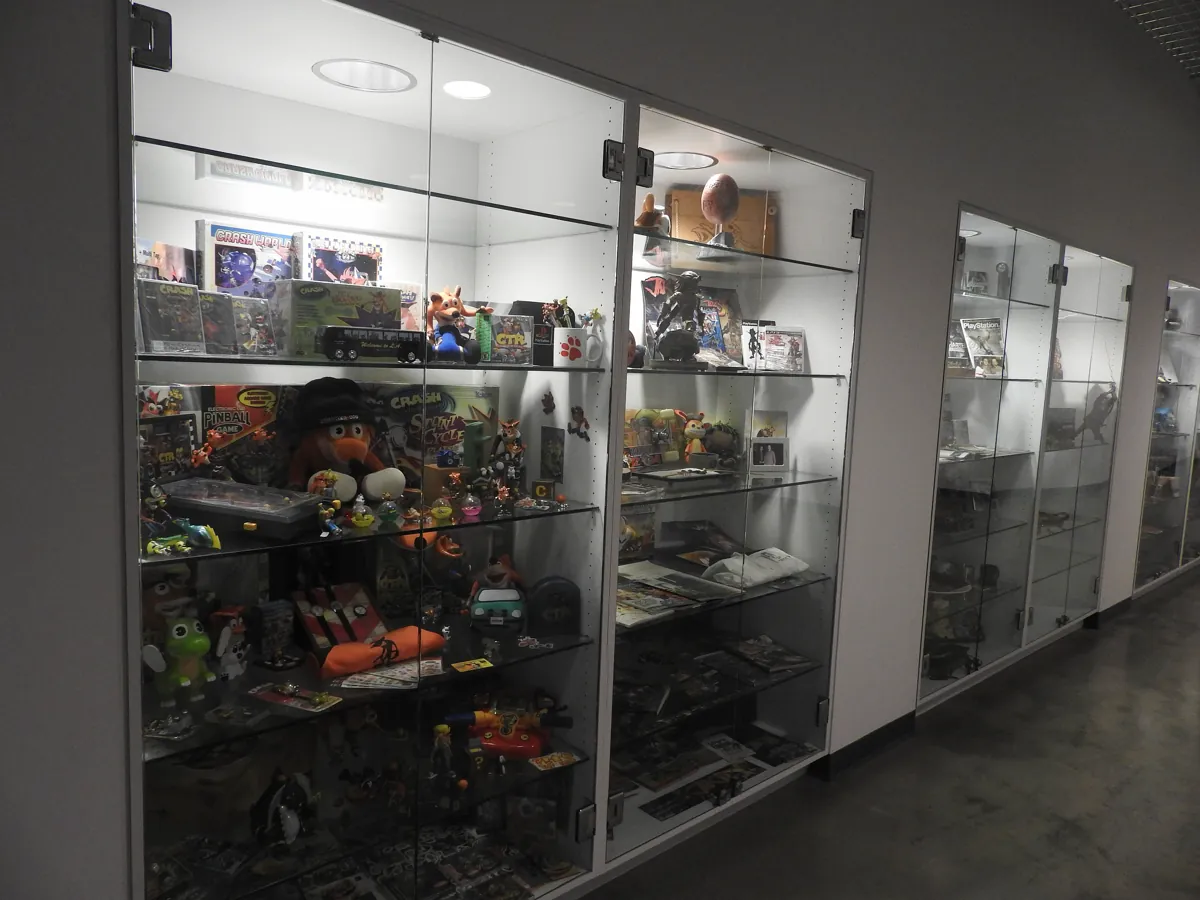 Glass display cases in a studio hallway filled with Crash Bandicoot boxes, figures and other Naughty Dog memorabilia