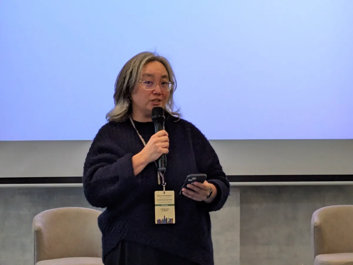 Selena Deckelmann speaking into a microphone in front of a projection screen at Wikimania 2025
