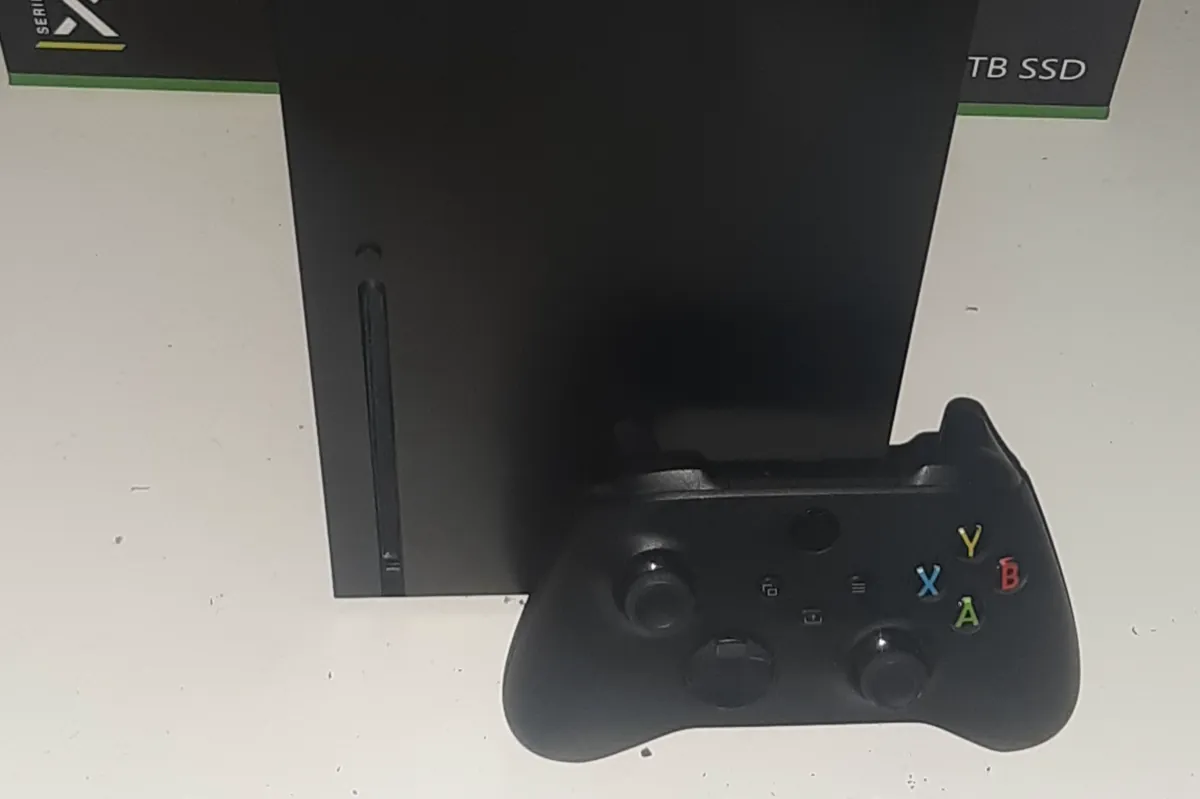 Front of a black Xbox Series X showing its vertical disc slot, with a black controller resting against it