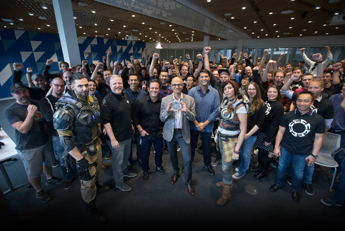 Satya Nadella holds up the Gears of War 4 gold master disc among cheering staff and cosplayers at The Coalition studio in 2016