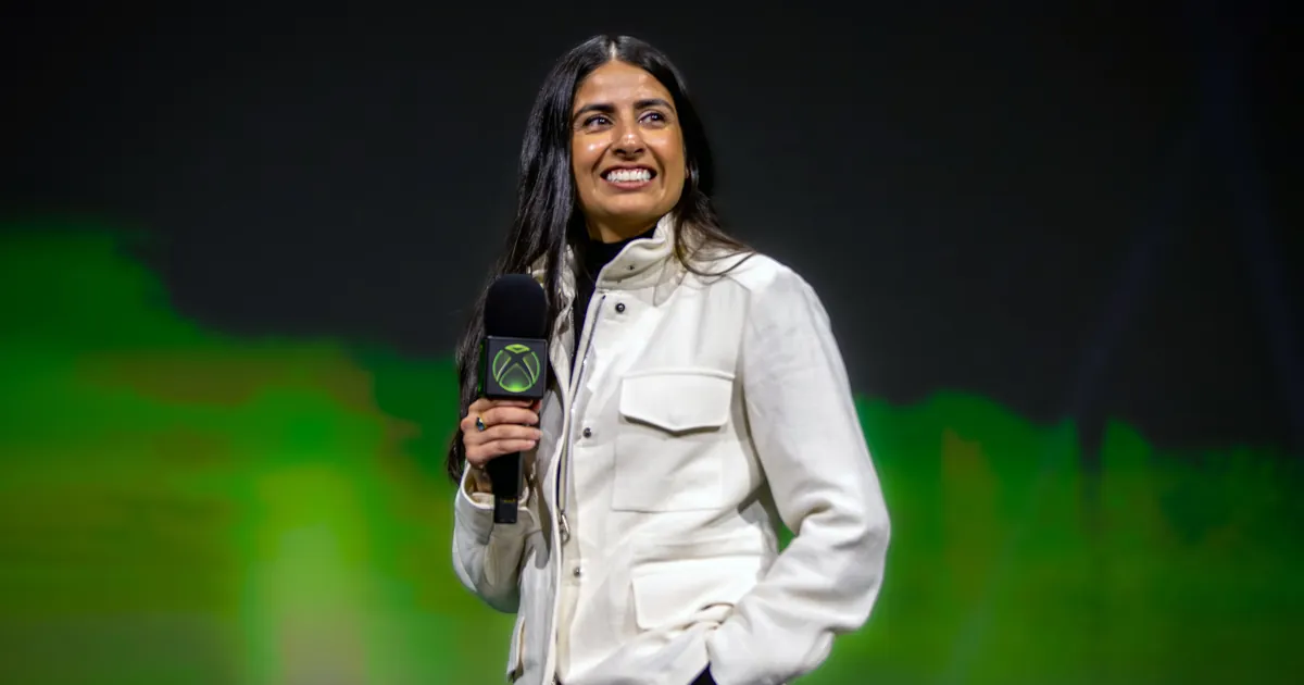 Xbox CEO Asha Sharma smiles on stage holding an Xbox-branded microphone at the 2026 Xbox Showcase