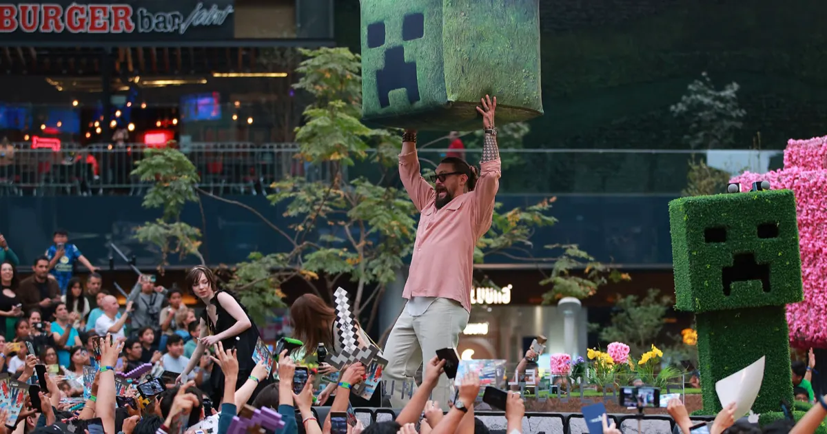 Jason Momoa lifts a giant Creeper head above a crowd of fans at a Minecraft Movie event